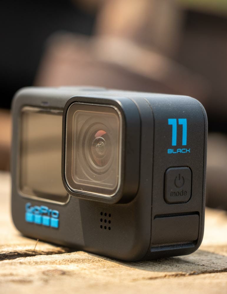 GoPro action camera on a wooden surface close up shot. Modern action camera with black body close up shot on a sunny day. GoPro 11 on a wooden table.