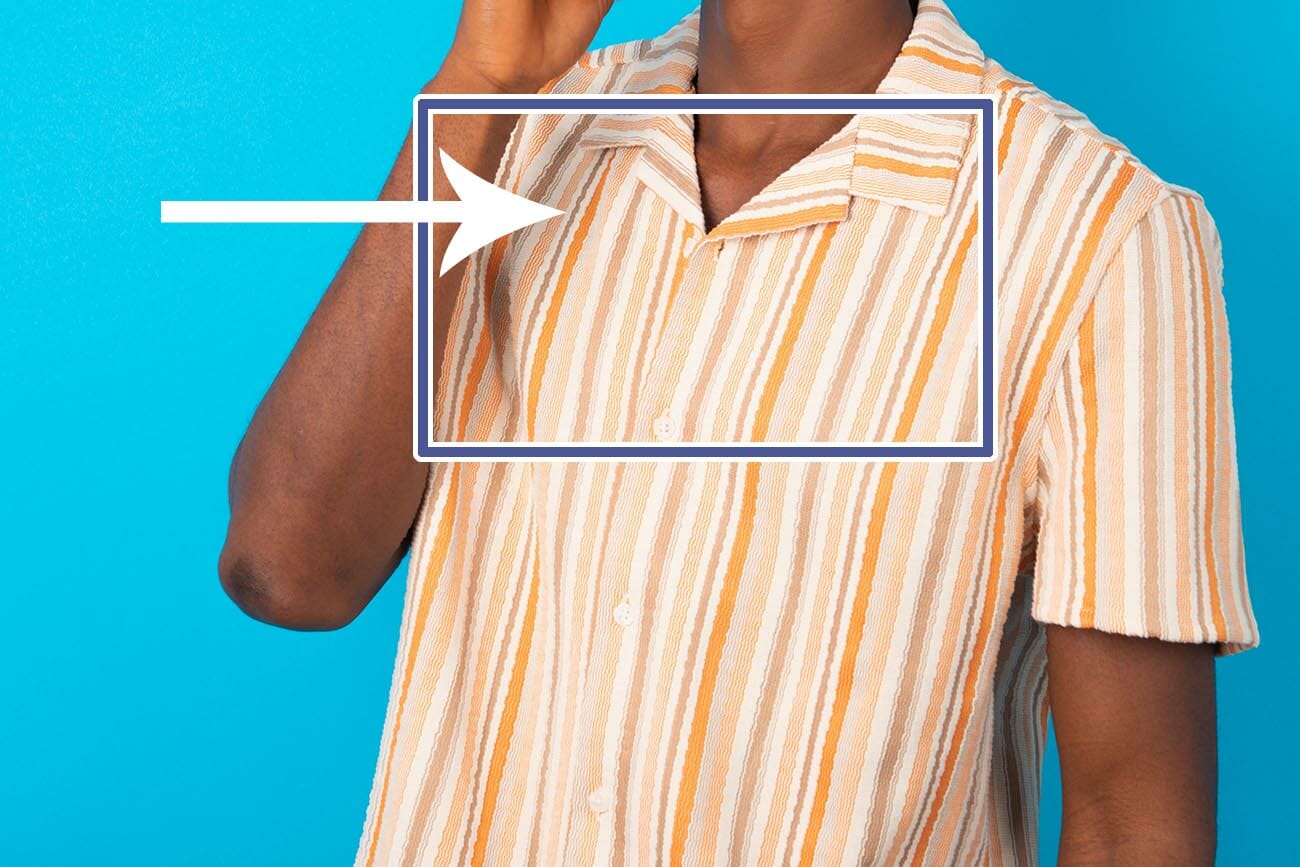 young man wearing Hawaiian striped shirt over blue background laughs happily keeps hand on chin expresses positive emotions smiles broadly has carefree expression