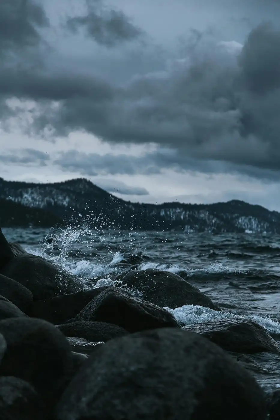 Waves crashing against rocks on the shore under a stormy sky
