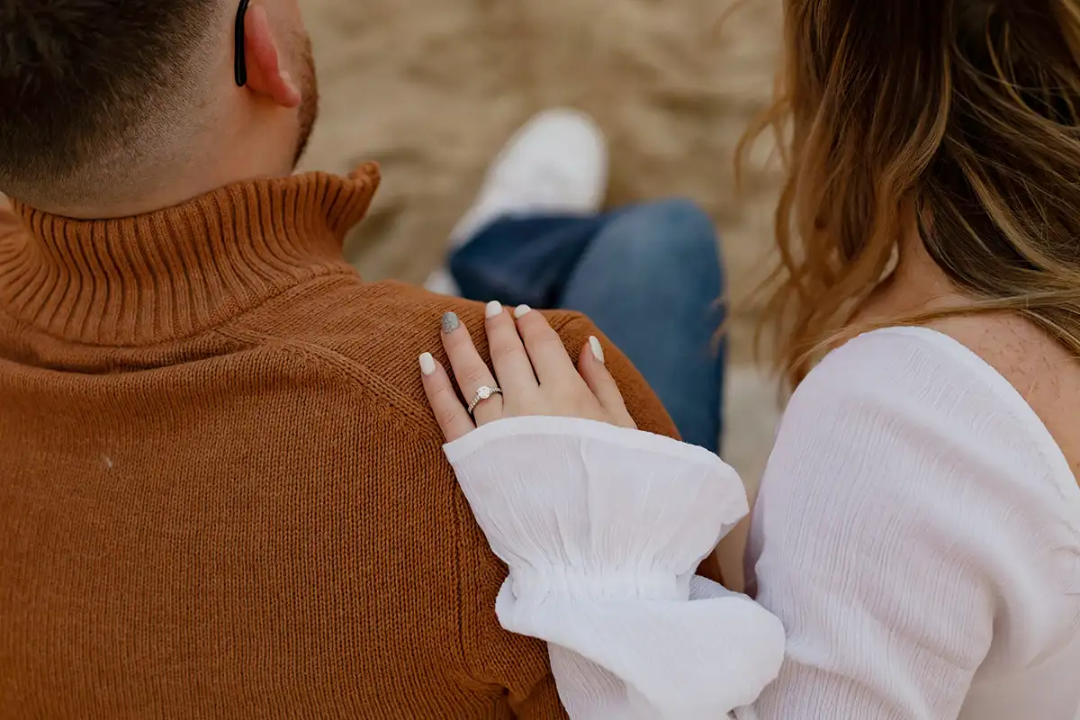 a womans hand with an engagement ring on the shoulder of a man sat next to her