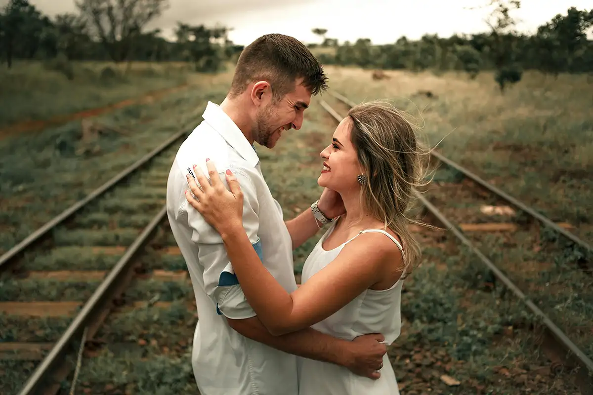a couple looking at each other, holding on to each other in the middle of two railtracks