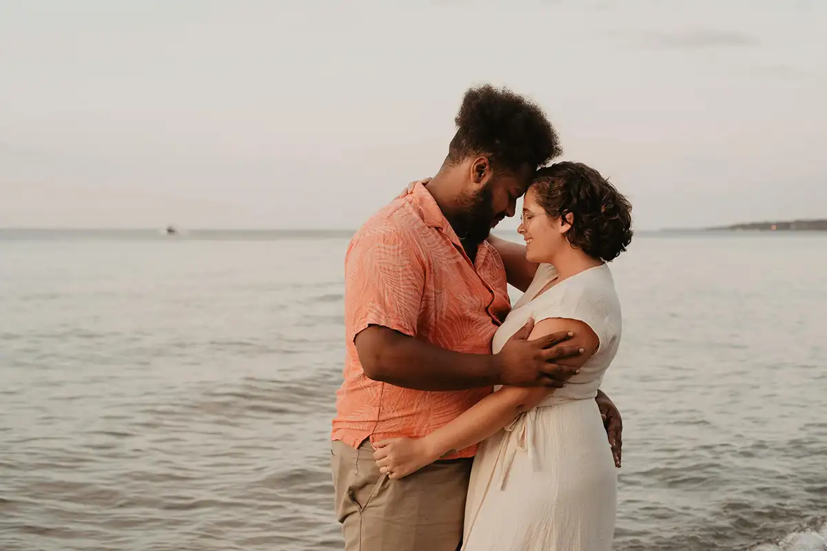 A black man cuddling a black woman in front of the sea