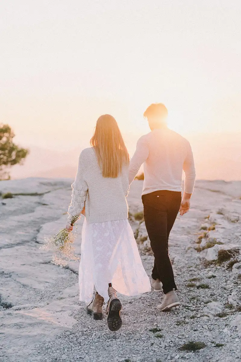 A couple walking towards the edge of a cliff at sunset