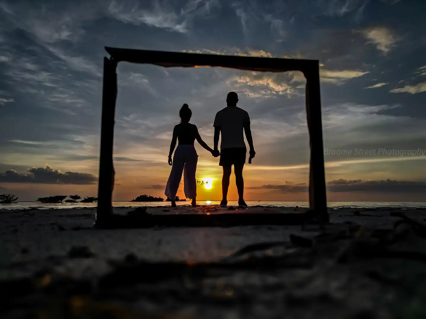 couple stood on a beach looking at a sunset with a frame around them