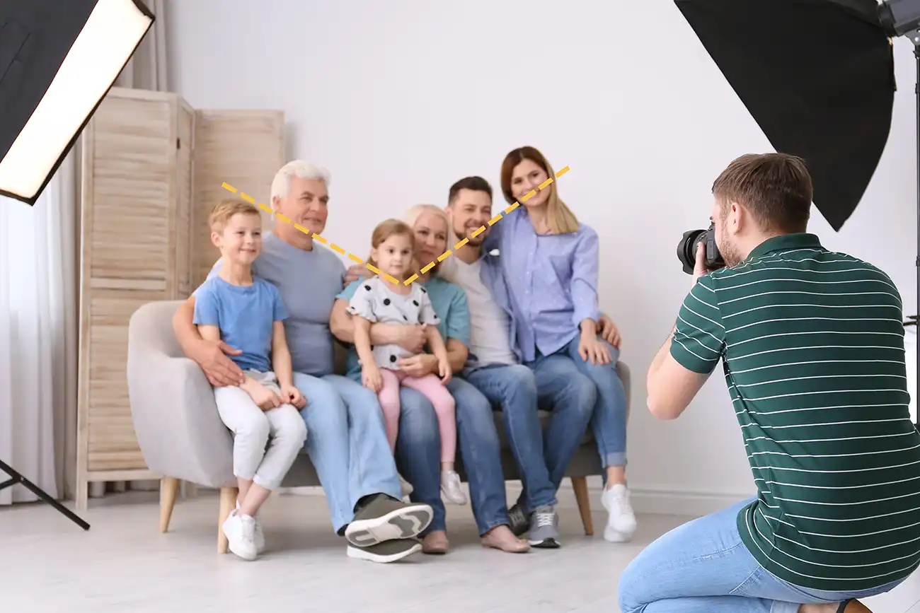 a family sat on a grey sofa cuddled together with children on their laps having their photos taken by a photographer with two lights either side of him